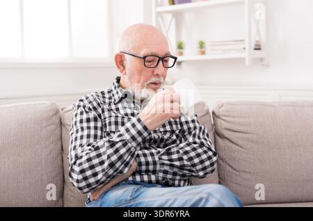 Older Man Enjoys a Warm Drink While Sitting on a Couch at Home During the Day Stock Photo