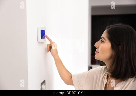 Young Hispanic woman regulating temperature on control panel indoors Stock Photo