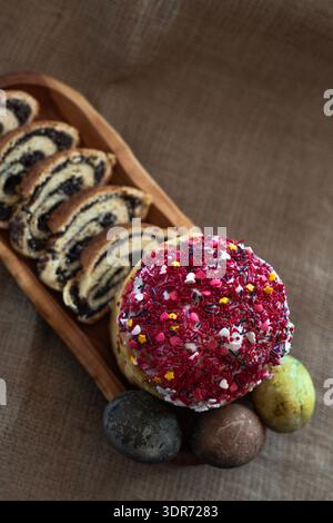 Overhead view of a festive Easter arrangement with three dyed eggs, homemade glazed Easter cake and neatly sliced poppy seed roll displayed on a long Stock Photo