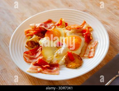 Delicious hearty dinner of sunny side eggs with baked potatoes and fried bacon pieces Stock Photo