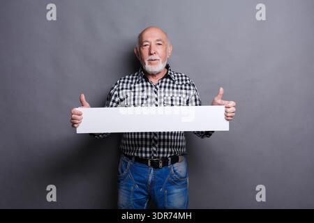 Senior Man Holds Blank Sign With Thumbs up in Studio Setting During Daytime Lighting Stock Photo