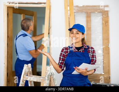 Happy Latin crafts woman in uniform making notes on the plan of an apartment during renovation Stock Photo