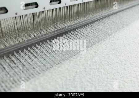 Closeup of boucle thread being woven on automated textile loom, ideal for fabric production, upholstery, and textile industry marketing visuals. Stock Photo