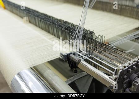 Closeup of automated loom weaving textile threads into fabric, ideal for manufacturing, textile industry branding, and industrial production marketing Stock Photo