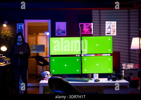 Man entering apartment, hacking using green screens PC, stealing credit card numbers and infiltrating banking systems. Hacker arriving in secret hideout, running code on mockup computer displays Stock Photo