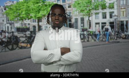 Man in white shirt pointing finger upward on street with crossed arms and serious gaze; confidence determination. Stock Photo