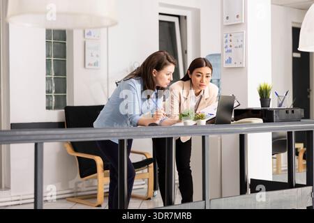 Businesswomen analyzing information on laptop and planning upcoming projects. Female marketing team reviews financial strategy using data reports and digital dashboards to guide company decisions. Stock Photo