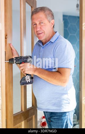 A focused middle-aged man using a screwdriver machine on wooden door at home Stock Photo