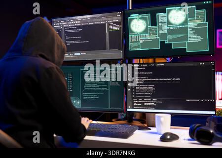 Cybercriminal coding on PC, creating stealth malware that evades security software. Hacker using programming language on computer to make script hiding malicious code from detection systems Stock Photo