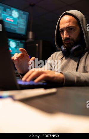 White man analyzing software solutions, coding and planning secure digital workflows. Caucasian male coder wearing sweatshirt hoodie, types steadily while reviewing technical interfaces on laptop. Stock Photo