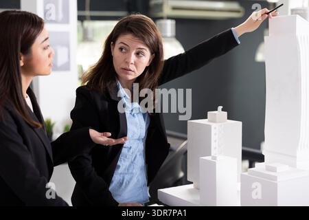 Female designers evaluate 3d printed building layout, checking for corrections and discussing improvements. Diverse women architects overseeing scale model in office, ready for client presentation. Stock Photo