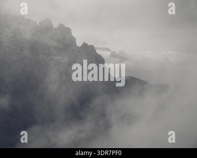 Dolomites, Italy - July 13 2025: Majestic mountain peaks emerging from dense fog and clouds in a dramatic grayscale landscape. Stock Photo