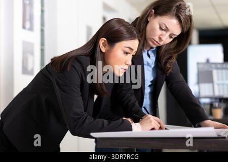 Diverse female professionals working on building designs and detailed floor plans for upcoming projects. Focused women architects collaborate closely while reviewing detailed blueprints in office. Stock Photo