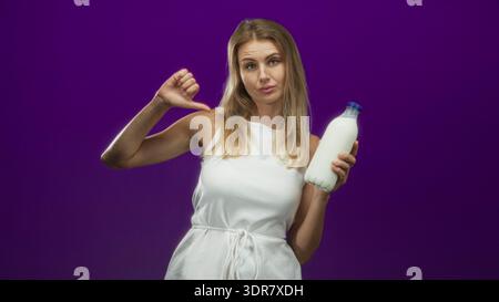 Woman holding milk bottle with screwcap, thumb pointing to chest and pouty expression, wearing white dress in studio; disapproval. Stock Photo