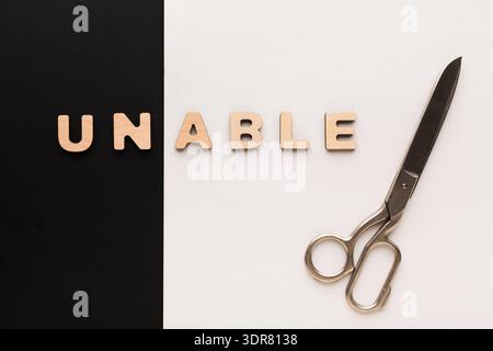 Scissors Placed Next to Wooden Letters Spelling Unable on a Contrasting Background Stock Photo
