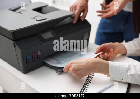 Office workers using printer at white desk indoors, closeup Stock Photo