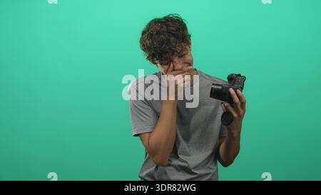 Man holding dslr camera, hand covering mouth and looking down in studio; creative frustration process. Stock Photo