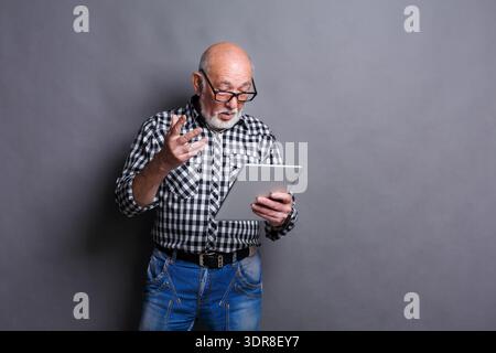 Senior Man Engaged in Reading on a Tablet in a Studio With Gray Background Stock Photo