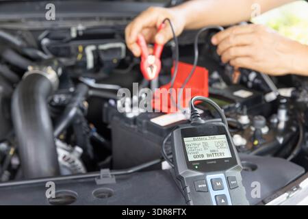 Man is measuring AGM battery power of suv car by battery tester at home. Stock Photo
