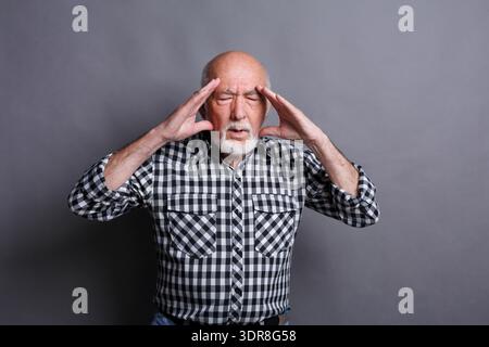 Man Holding His Head in Pain Standing Against a Gray Background in a Checkered Shirt Stock Photo