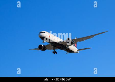 An aircraft glides through a clear blue sky, preparing to land at YVR airport.  The aircraft's sleek design is highlighted by sunlight as it descends. Stock Photo