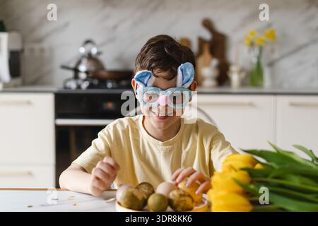 Smiling child wearing bunny ears with natural Easter eggs at home kitchen Stock Photo