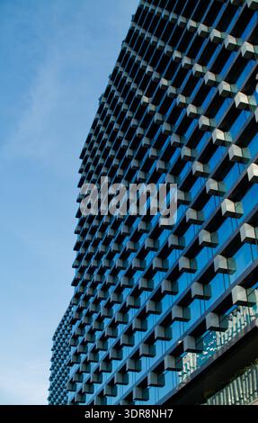 Modern skyscraper with geometric glass facade featuring diamond pattern. Contemporary tower with reflective blue surface and architectural detail. Stock Photo