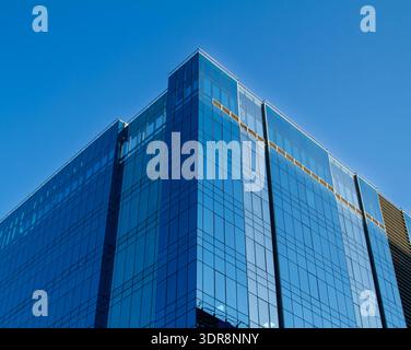 Contemporary glass skyscraper with dynamic angular design reflecting blue sky. Modern corporate tower with striking architectural form. Stock Photo