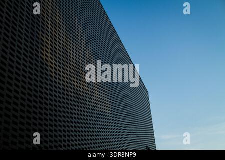 Contemporary glass building with dramatic silhouette against deep blue sky. Modern architecture with strong geometric form and minimal detail. Stock Photo