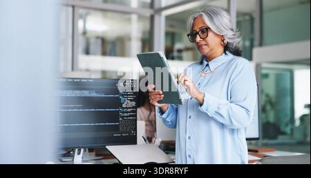 Woman, reading and tablet for programming in office for research, software manual and coding. Mature person, space and troubleshooting with digital Stock Photo