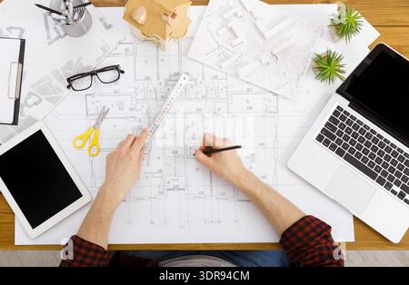 Person Working on Architectural Plans With Tools and Technology on a Wooden Desk Stock Photo