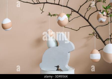 Tree branches with Easter eggs and decorative rabbit near beige wall Stock Photo
