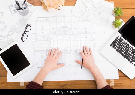 Hands of a Person Working on Architectural Plans in an Office Setting With a Laptop and Tablet Stock Photo