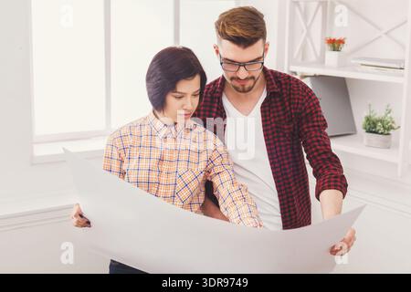 Couple Looks at Large Paper Plans in a Bright Room During the Afternoon Stock Photo