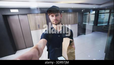 Delivery man, ring bell and package at front door with pov, service and ecommerce with glass in lobby. Person, courier and paper bag with order Stock Photo