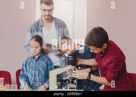 Children Learn About Science in Classroom With Microscope and Teacher Guiding Them Stock Photo