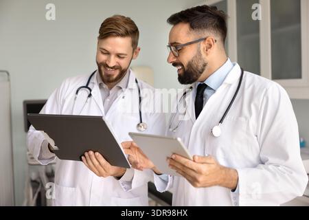 Friendly smiling male doctors discuss diagnosis using paper electronic documents Stock Photo