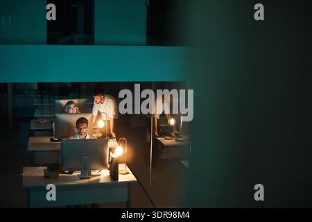 Night, computer and coworking with business people in office for fact check, typing or review news. Tech, reading and team of journalists in workplace Stock Photo
