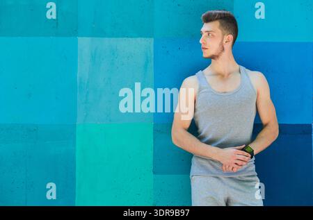 Young Man Stands Against a Blue-Green Wall While Holding a Watch During Daylight Hours Stock Photo