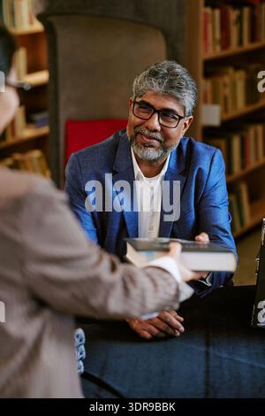 Middle Aged Man Smiling While Handing Book during Presentation Stock Photo