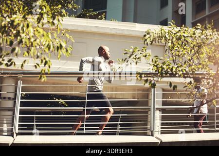 Athlete, black man and running for fitness in city for exercise, training and physical activity. Serious, male person and bridge with speed challenge Stock Photo