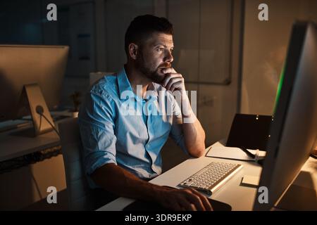 Night, computer and thinking with business man in office for planning, research and it web system. Overtime, vision and project manager with employee Stock Photo