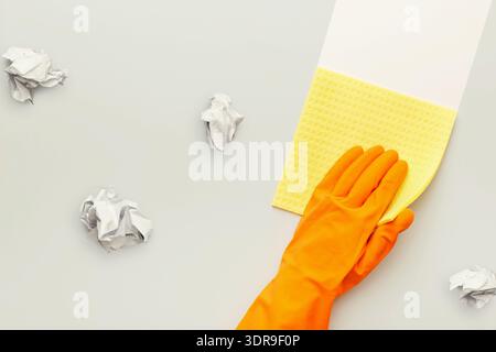 Cleaning Process With Yellow Sponge and Orange Glove on Light Surface With Crumpled Paper Stock Photo
