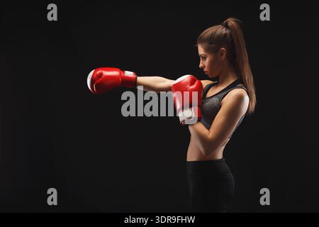 Young Woman Practices Boxing Technique With Red Gloves in Dark Setting Stock Photo