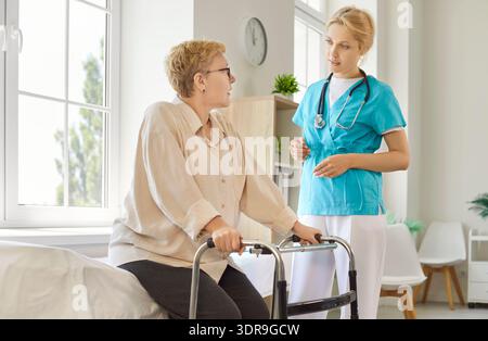 Senior patient using walker, nurse standing by to assist and help old woman Stock Photo