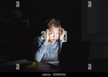 Feeling Stressed While Working on a Laptop in a Dark Room at Night Stock Photo