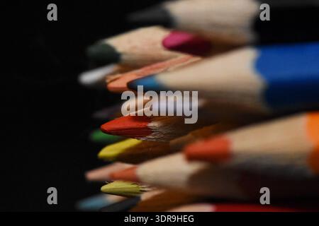 Macro close-up of a stack of sharpened colored pencils showing various wood textures and vibrant lead tips against a black background. Stock Photo