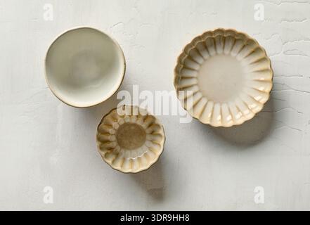 Top view of three empty decorative small ceramic bowls placed on a light painted kitchen table surface. Minimal and cozy composition suitable for kitc Stock Photo