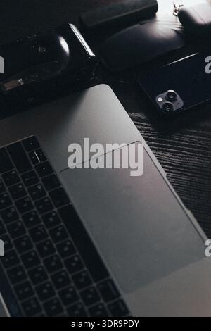 Close-up of workspace with laptop smartphone and gadgets in dark aesthetic. Stock Photo