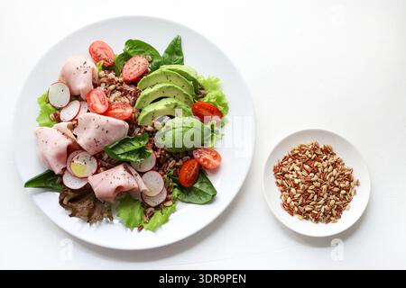 Fresh and healthy mixed grain salad with avocado, sliced ​​turkey or chicken, cherry tomatoes, radishes, fresh lettuce leaves, and baby spinach. Stock Photo